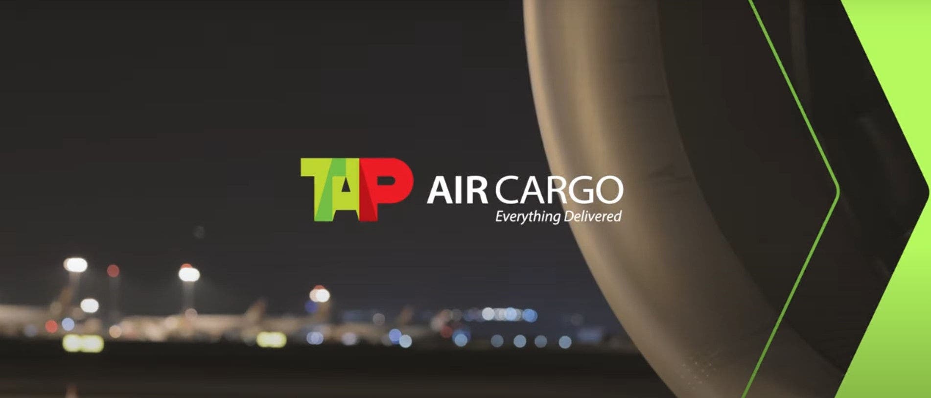 Frame TAP Air Cargo, ramo da TAP especializado em transporte de carga aérea. O fundo é escuro, tratando-se de um aeroporto à noite. No centro da imagem está o logotipo da TAP, sendo visível à direita a estrutura de um motor de avião.